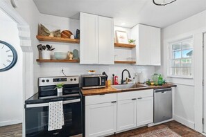 A modern kitchen with white cabinetry, a microwave, a stove, and a sink.