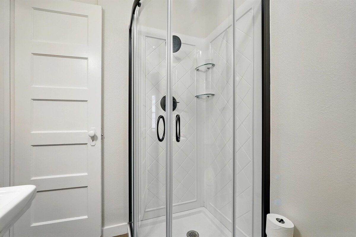 A bathroom with a white door, a glass shower enclosure, and a toilet paper holder.