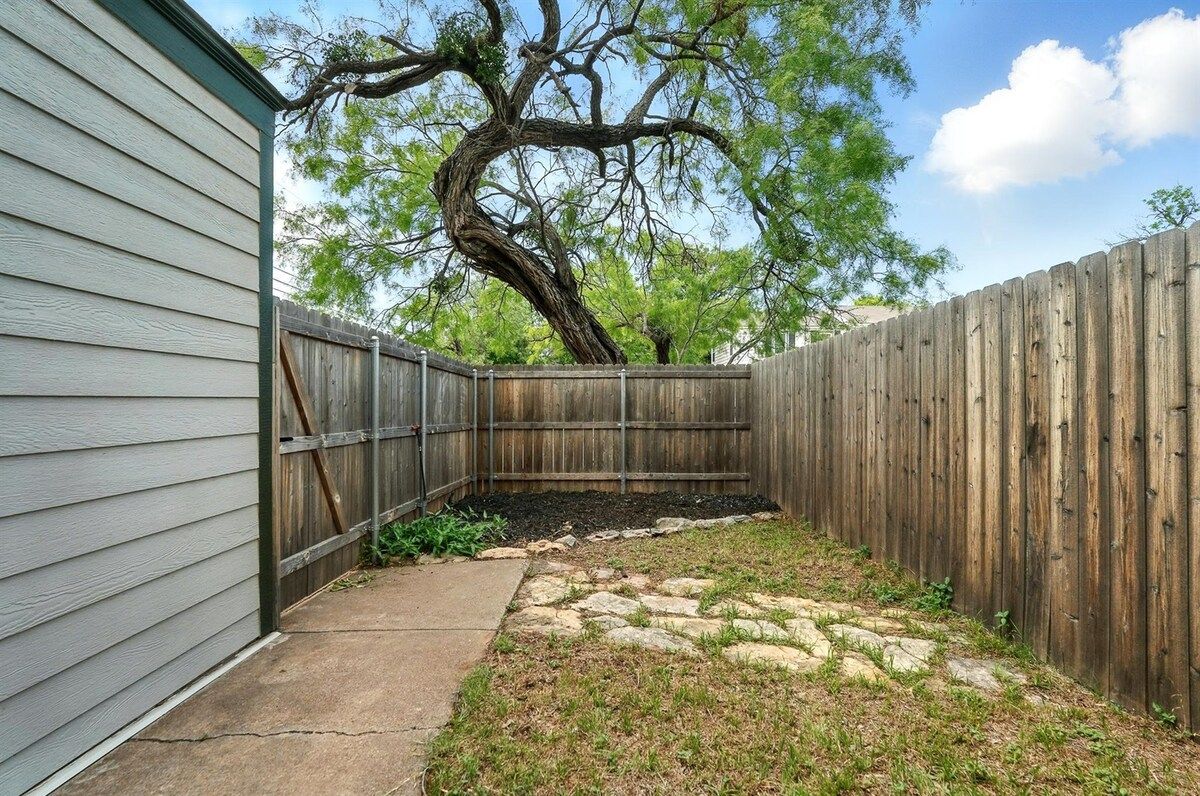 A backyard with a wooden fence, a tree, and a stone pathway.