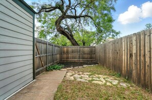 A backyard with a wooden fence, a tree, and a stone pathway.
