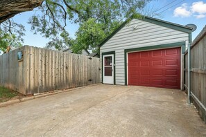 A garage with a red door, a wooden fence, and a tree overhead.