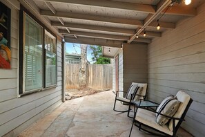 A covered patio area with a concrete floor, two chairs, and a wooden fence in the background.