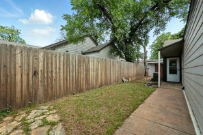 A backyard with a wooden fence, a grassy area, and a concrete pathway leading to a house.