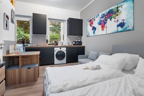 Una habitación de hotel moderna con una cama, un escritorio con una silla, una lavadora y una zona de cocina.