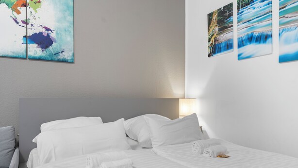 A hotel room with a bed, pillows, and a wall with artwork. - Apartment Cologne City (köln)