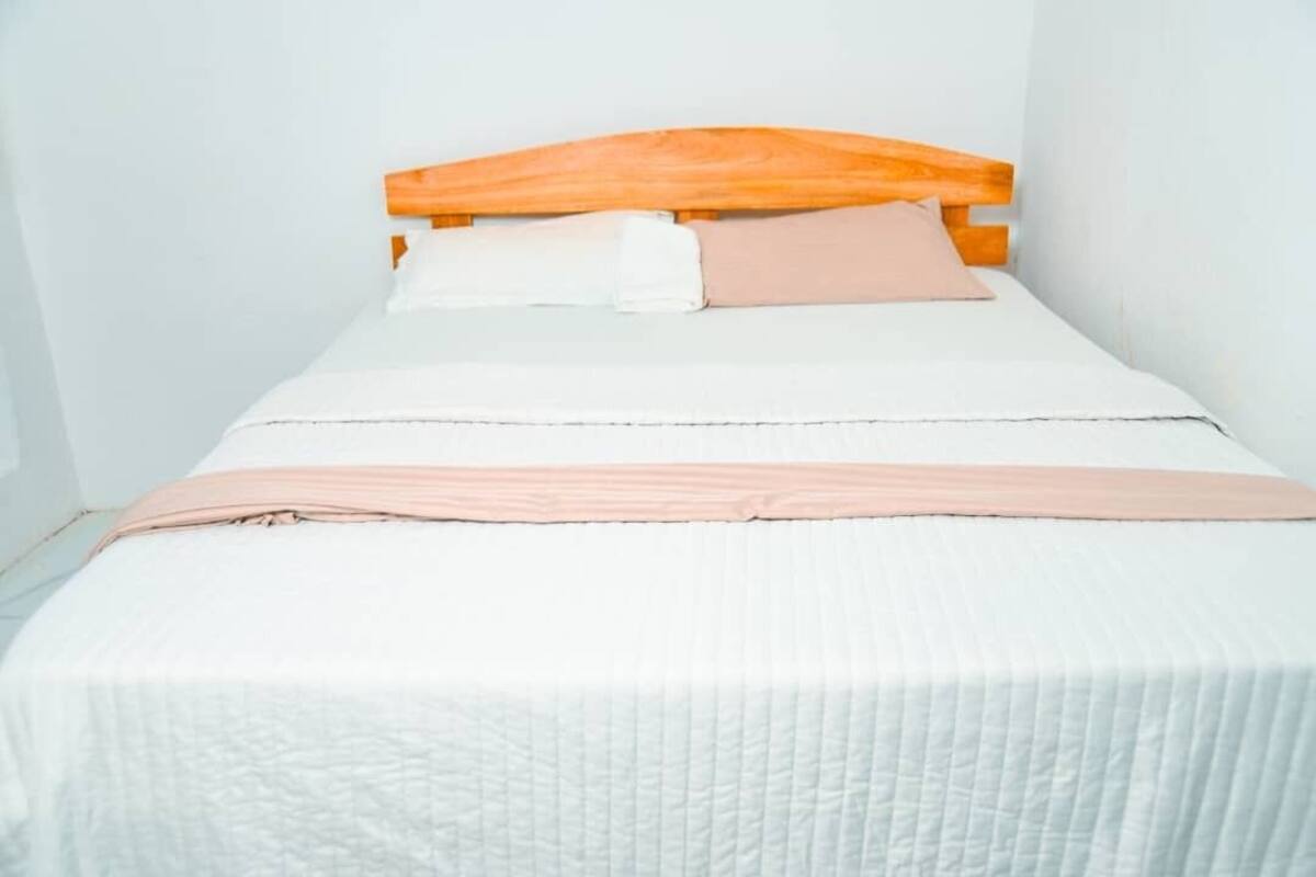 A small, single-bed room with a wooden headboard, white bedding, and a pink blanket.