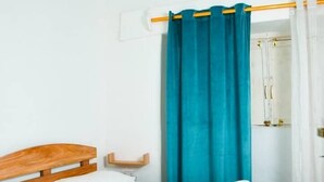 A bedroom with a wooden bed, white bedding, a teal curtain, and a ceiling fan. - Breflection Spa and Hostel (Zanzibar Town)