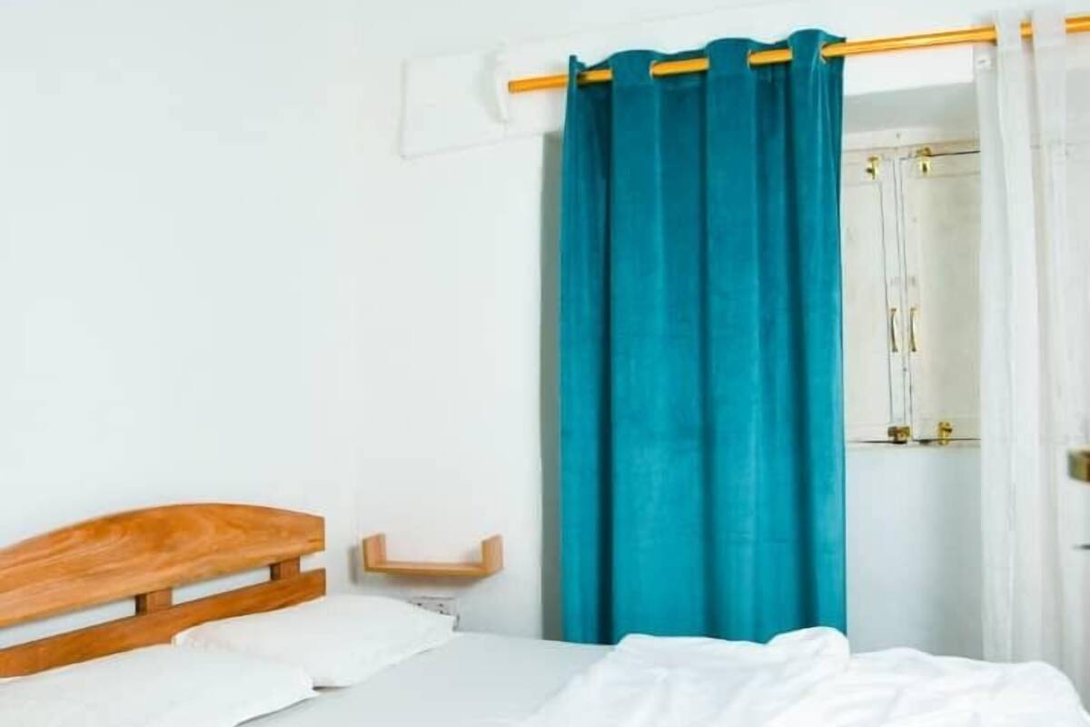 A bedroom with a wooden bed, white bedding, a teal curtain, and a ceiling fan.