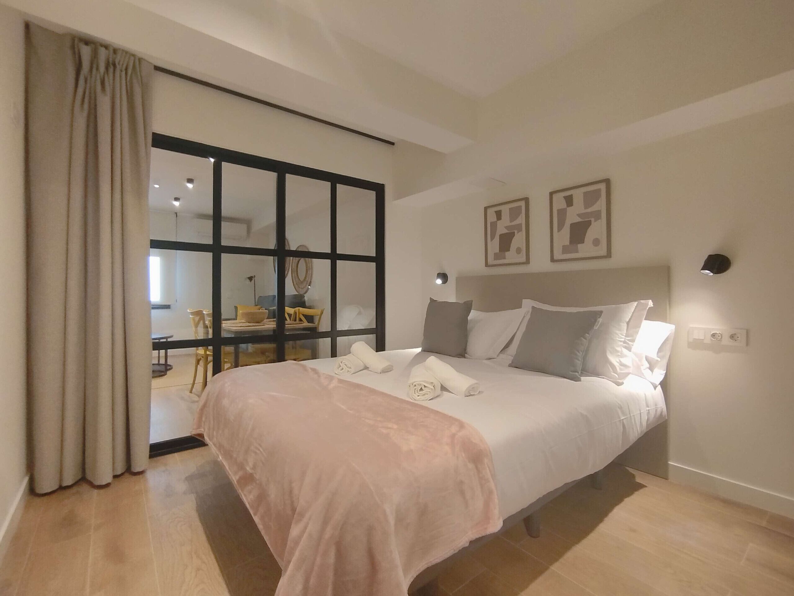 Une chambre dotée d’un grand lit, d’une porte-fenêtre coulissante donnant sur un coin repas et d’un luminaire fixé au mur.