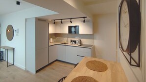 Une cuisine moderne équipée d’un four encastré, d’un four à micro-ondes et d’une machine à café. On y trouve une table à manger en bois, agrémentée de deux sets de table en fibres tressées.