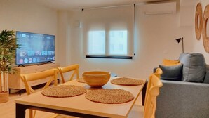 Un salon moderne comprenant une table à manger, des chaises, un téléviseur, un canapé et une fenêtre.