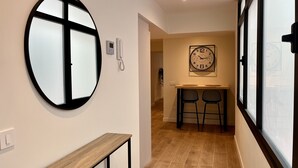 Un couloir avec un grand miroir rond, un téléphone fixé au mur, une horloge et une petite table avec des chaises.