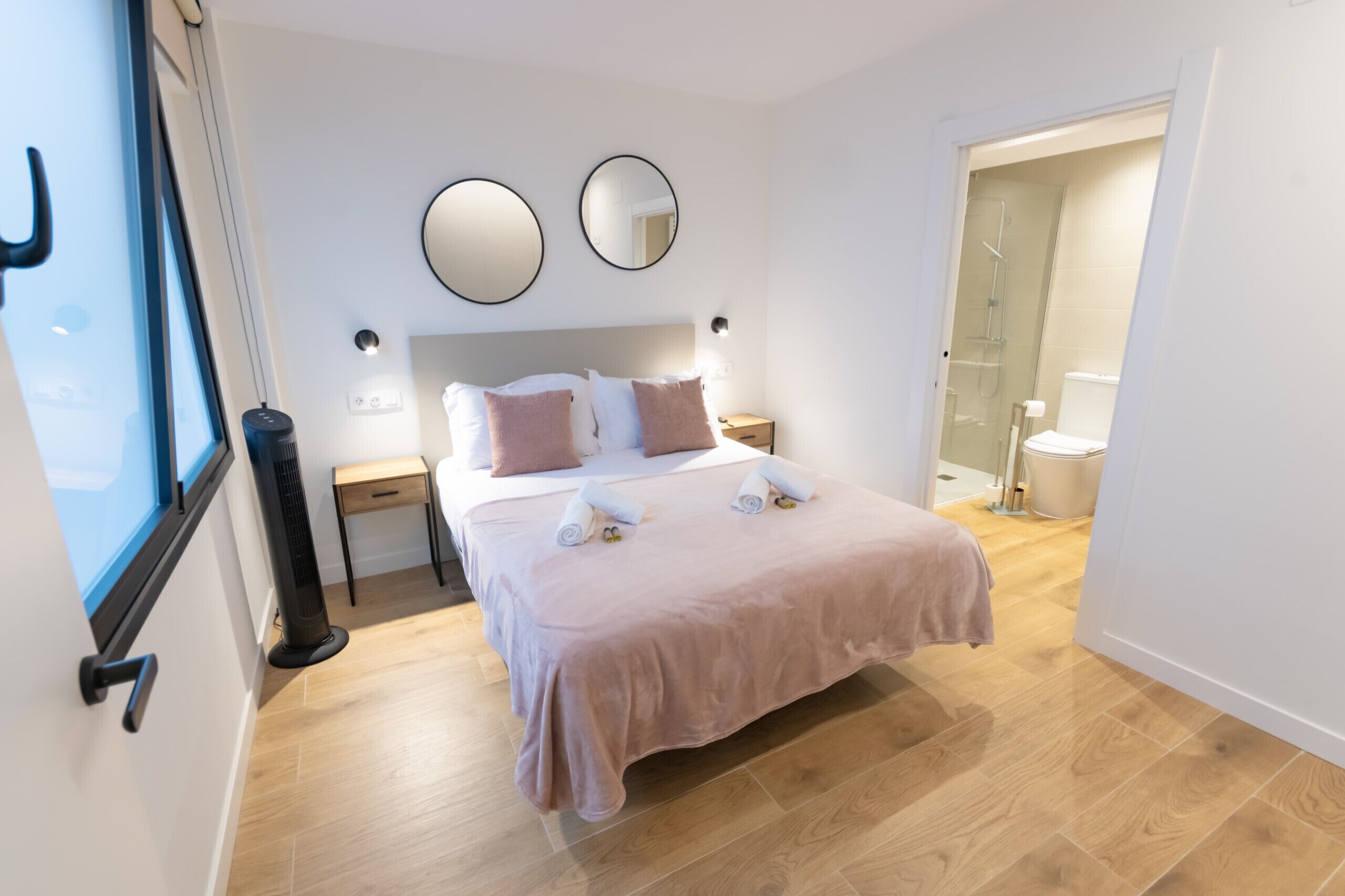 A modern bedroom with a large bed, two bedside tables, a bedside lamp, a mirror, and a view of a bathroom.