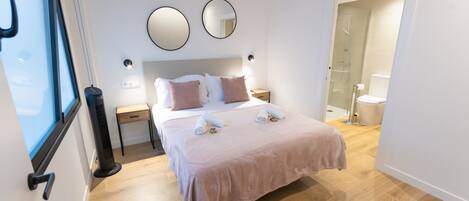 A modern bedroom with a large bed, two bedside tables, a bedside lamp, a mirror, and a view of a bathroom.