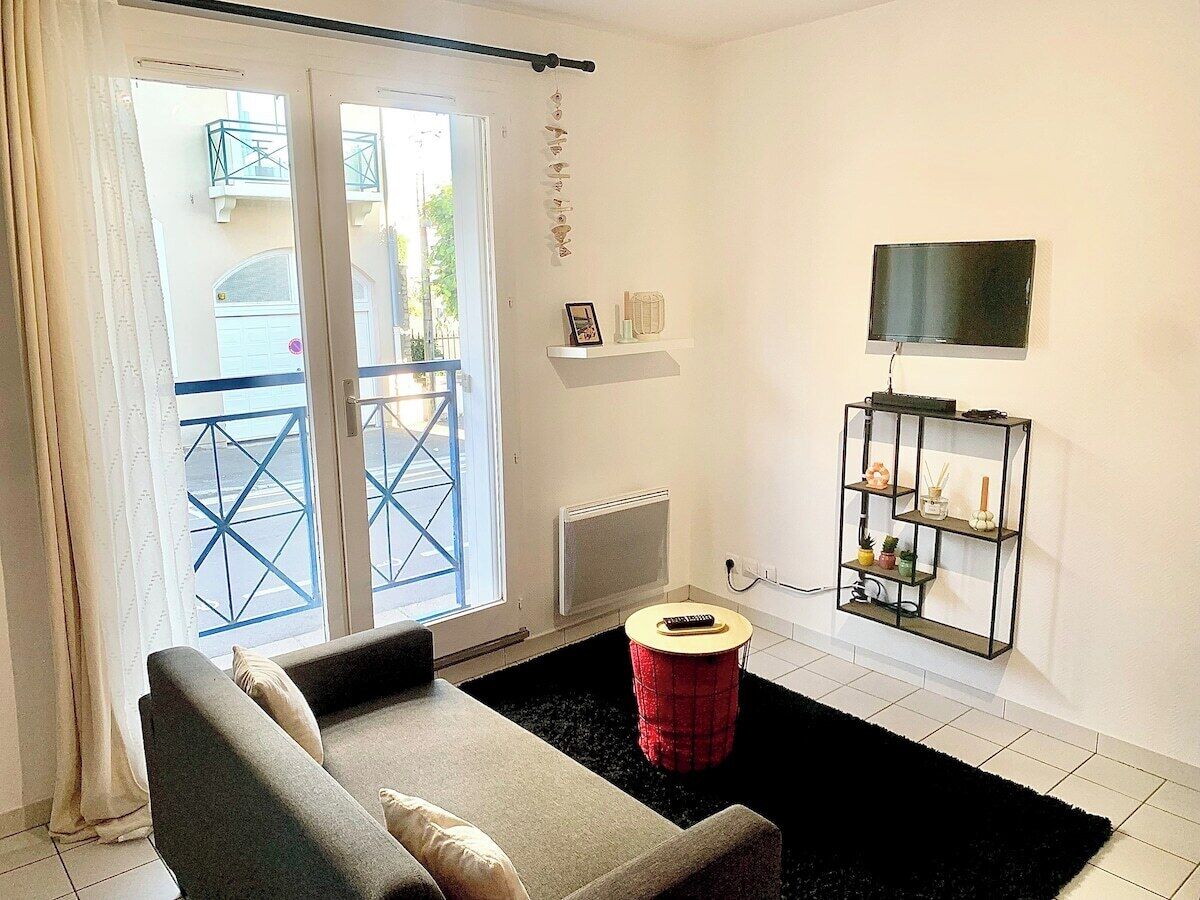 A living room with a sofa, a red stool, a TV, and a shelf with plants.