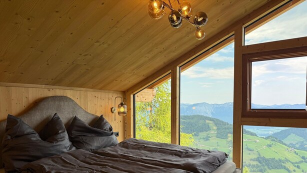 Ein Schlafzimmer mit einem großen Bett, einer Holzbalkendecke und einem Fenster mit Blick auf die Berge.