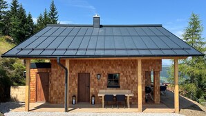 Eine Holzhütte mit einem Metall-Dach, einer Holztür, einem Fenster und einem Tisch mit Stühlen davor.