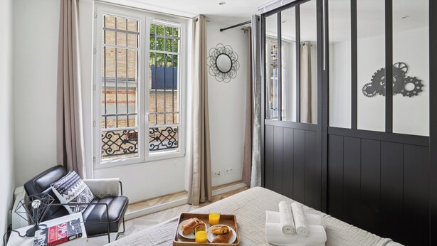 A hotel room with a bed, a chair, a tray with breakfast, a window with curtains, and a decorative mirror. - Modern Central Paris Flat by Les Halles (Paris)