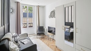 A modern living room with a sofa, a chair, a small table, and a TV. There is a sliding door leading to an outdoor area. - Modern Central Paris Flat by Les Halles (Paris)
