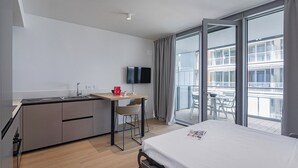 A modern hotel room with a bed, a small kitchenette, a dining area, and a balcony with a view of the city. - Waterfront Blue by Wonderful Italy (Genova)