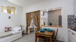 A modern living room with a sofa, a dining table with chairs, and a kitchen area with a sink and countertop.