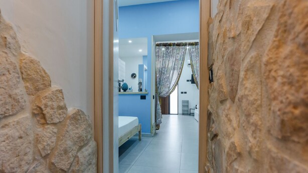 A narrow hallway with a stone wall on one side and a bathroom with a blue wall and white floor tiles.