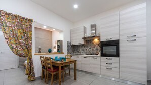 A modern kitchen with white cabinets, a wooden dining table, and a colorful curtain.
