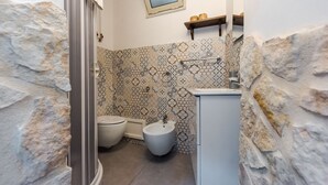 A bathroom with a stone wall, a toilet, a bidet, and a sink.