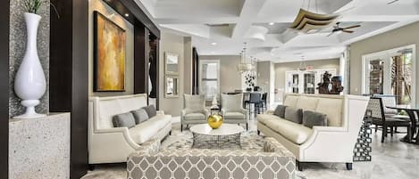 A spacious living room with a modern design, featuring a large sofa, a coffee table, and a dining area with a chandelier.