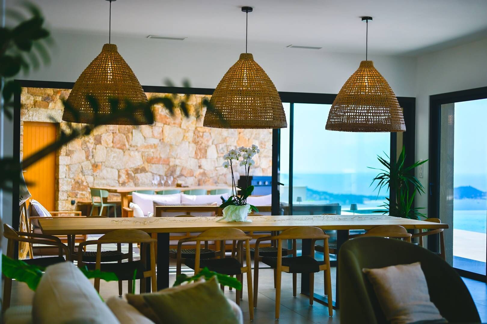 A dining area with a large table, wicker pendant lights, and a view of the ocean.