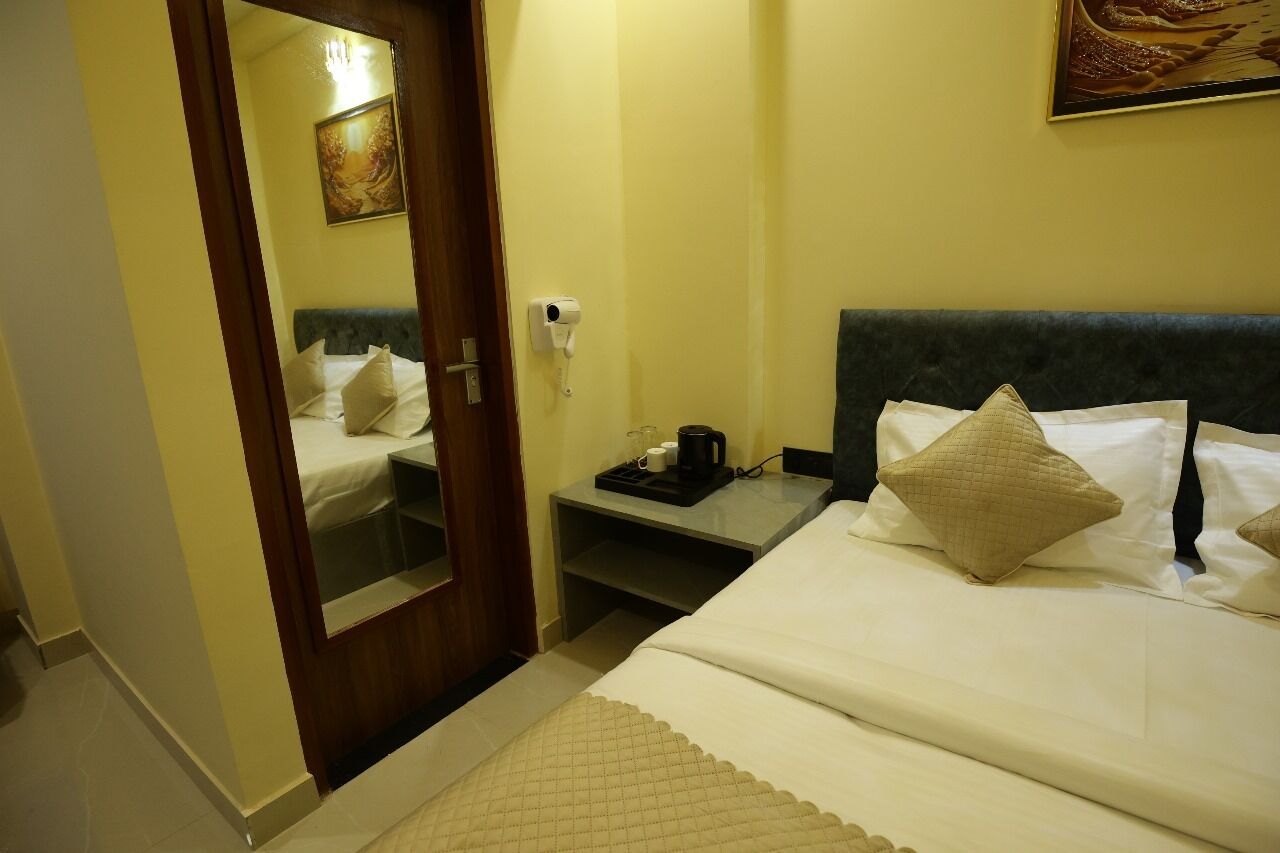 A hotel room with a bed, a nightstand, a mirror, and a painting on the wall.