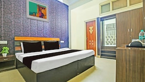 A bedroom with a bed, a nightstand, a potted plant, a wardrobe, and a door with a curtain. - Hotel Kingstone Zirakpur (Zirakpur)