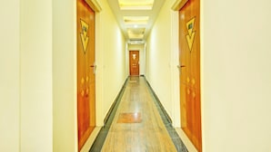 A long, narrow hallway with wooden doors on both sides, leading to a central door at the end. - Hotel Kingstone Zirakpur (Zirakpur)