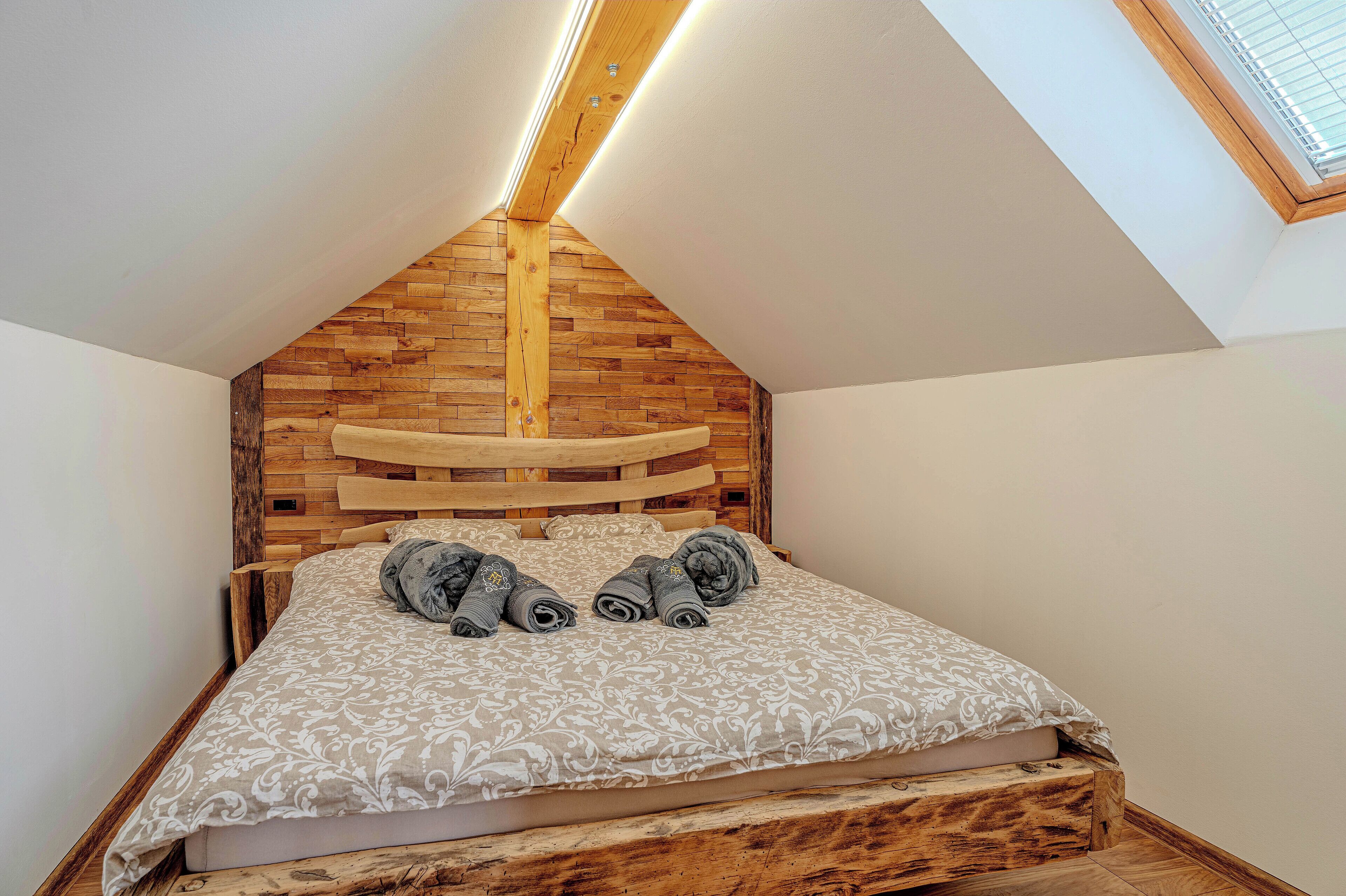 Una camera da letto con soffitto a falde, testiera in legno e finestra sul tetto.