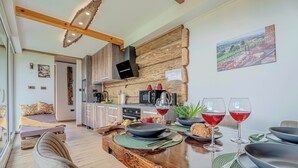 A modern kitchen with wooden accents, a dining area with a wooden table set for two, and a bed with a view. - Vineyard cottage Pri mali luži (Mokronog-Trebelno)
