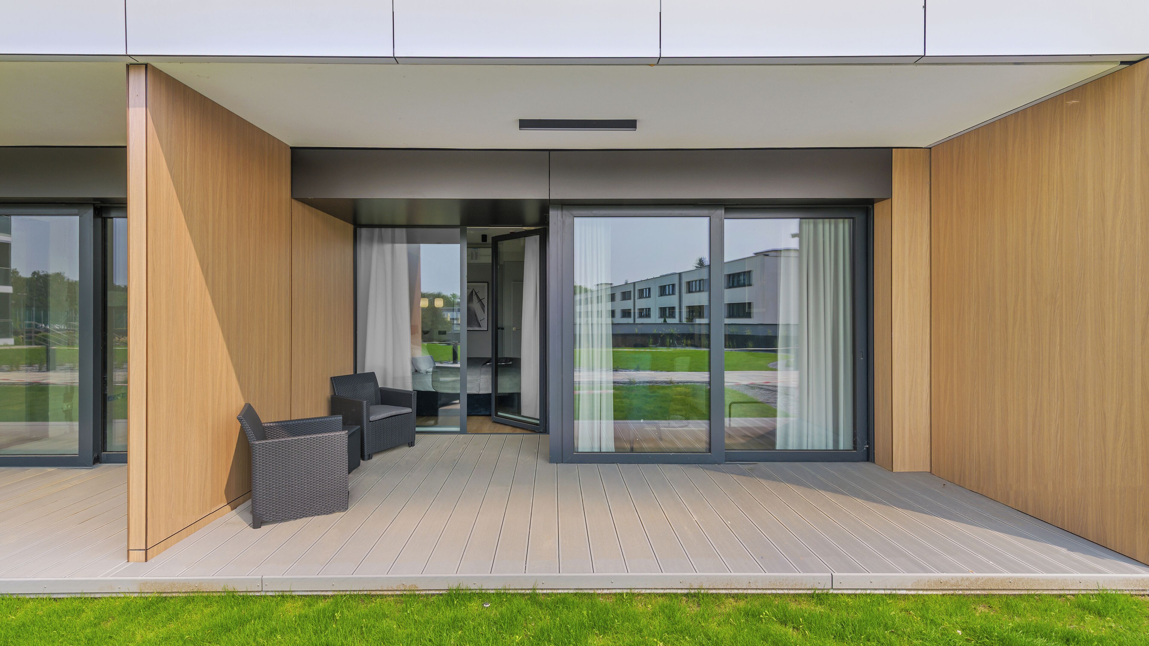 A modern building with a wooden exterior, large sliding glass doors, and a patio area with outdoor furniture.