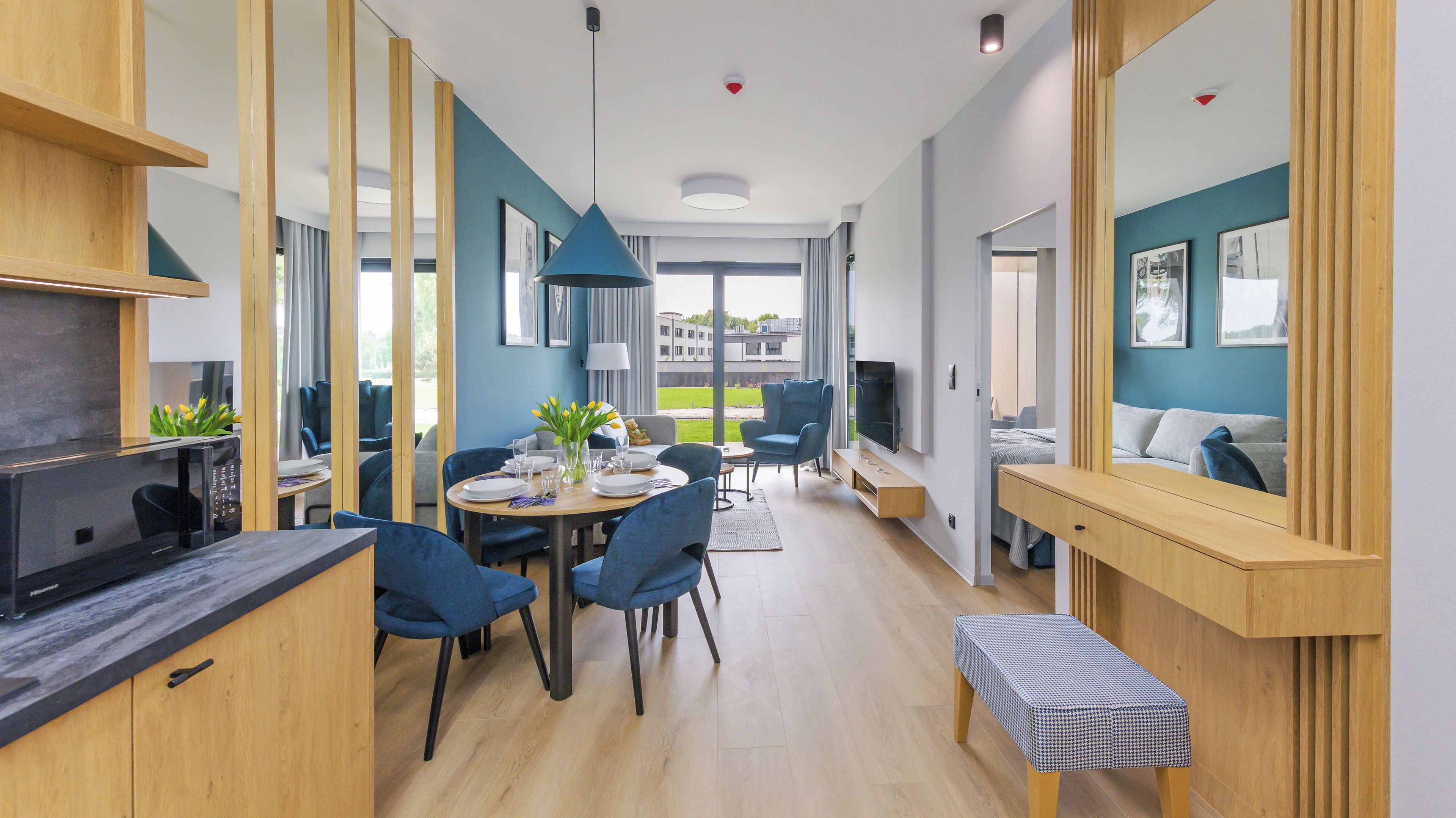 A modern dining area with a wooden table, blue chairs, and a view of the outdoors.