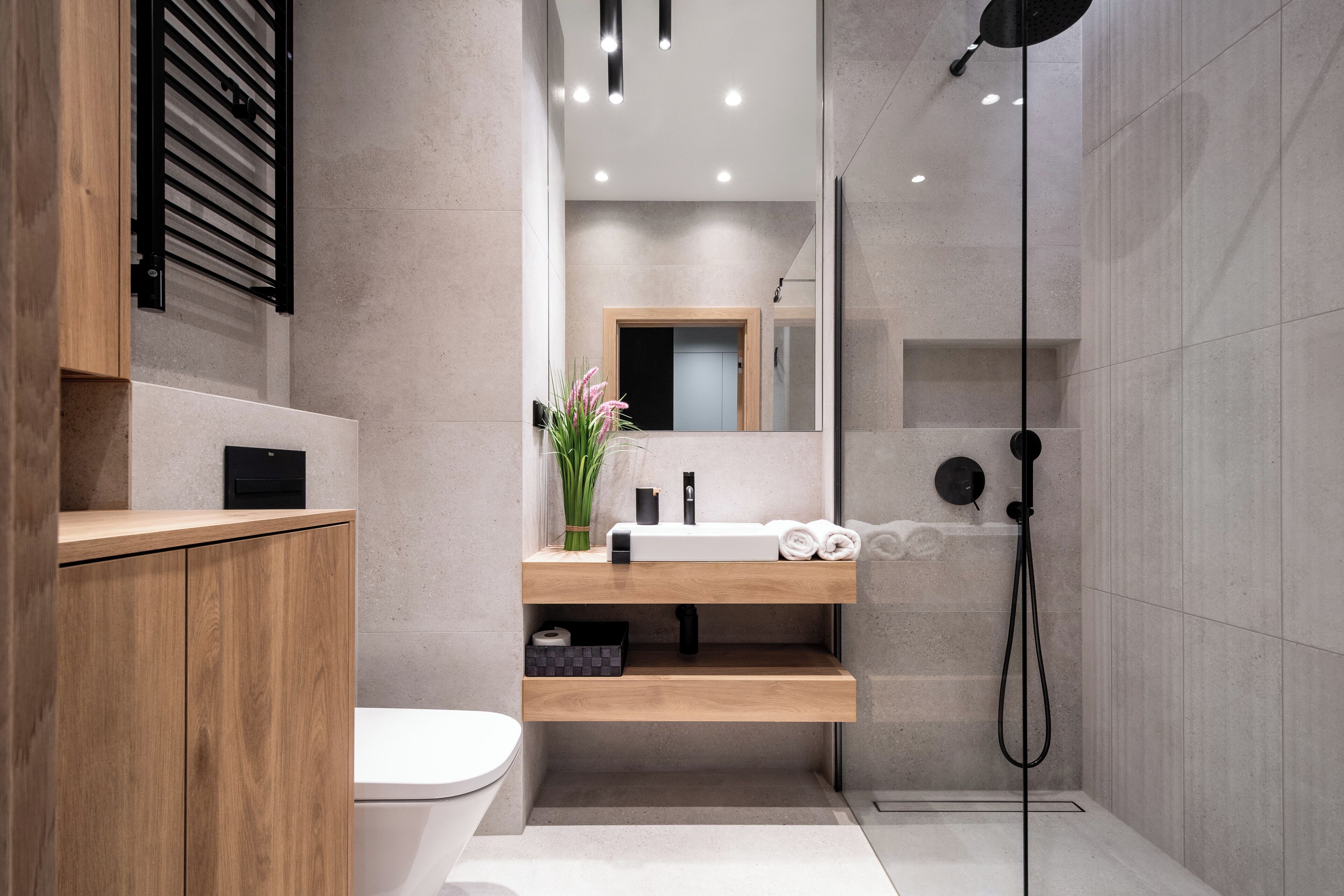 A modern bathroom with a wooden vanity, a toilet, a sink with a mirror, and a shower.