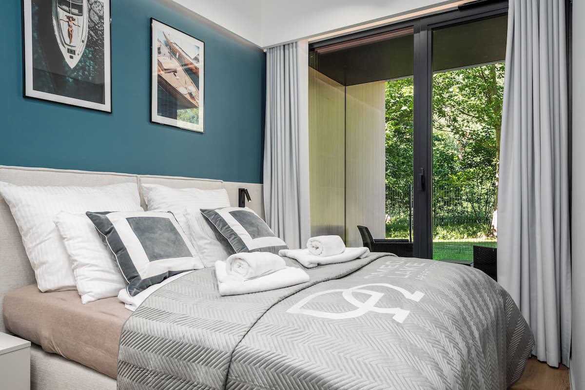 Une chambre avec un grand lit, une table de chevet et une vue sur la verdure par la fenêtre.