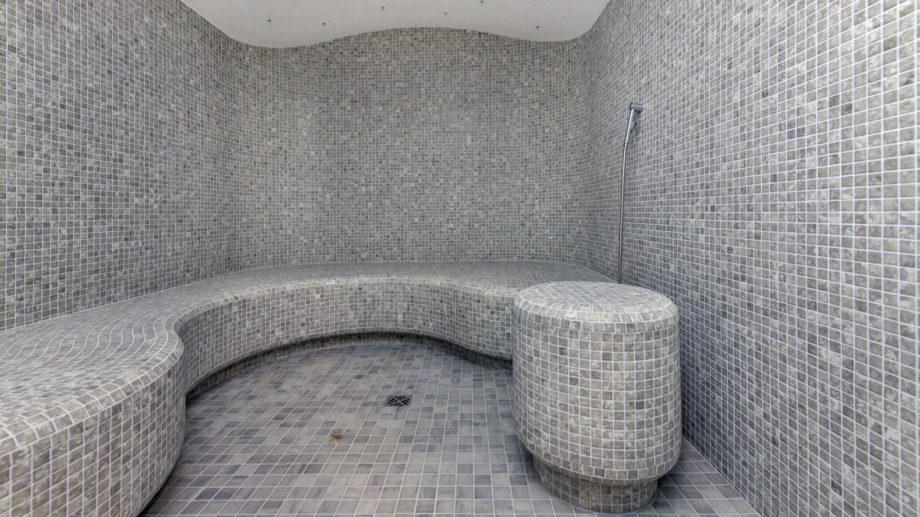 Un baño con paredes y piso de mosaicos, un banco curvo y una zona de ducha.