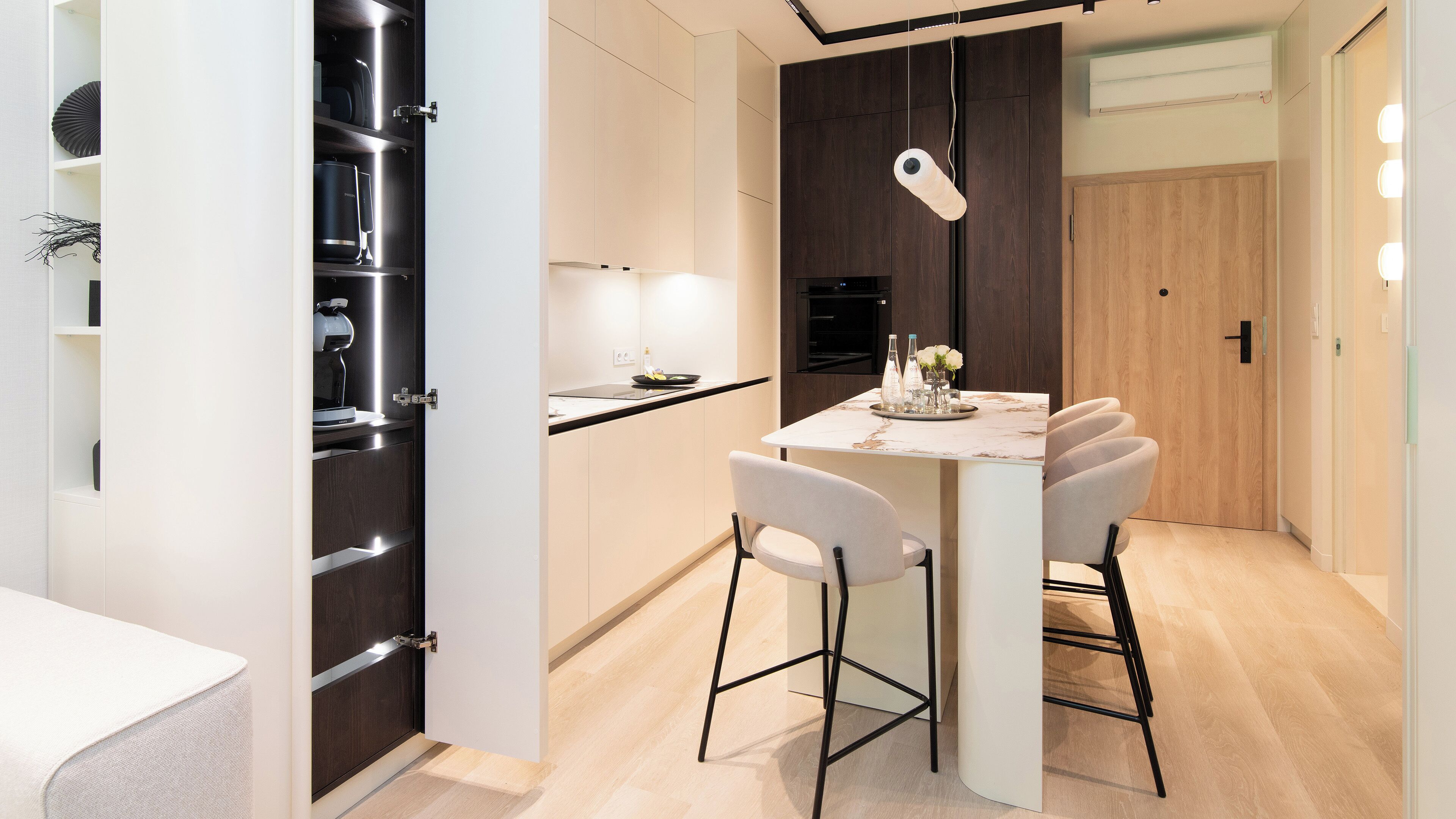 Une cuisine moderne avec un coin repas, comprenant un plan de travail en marbre, des chaises blanches et un four encastré.