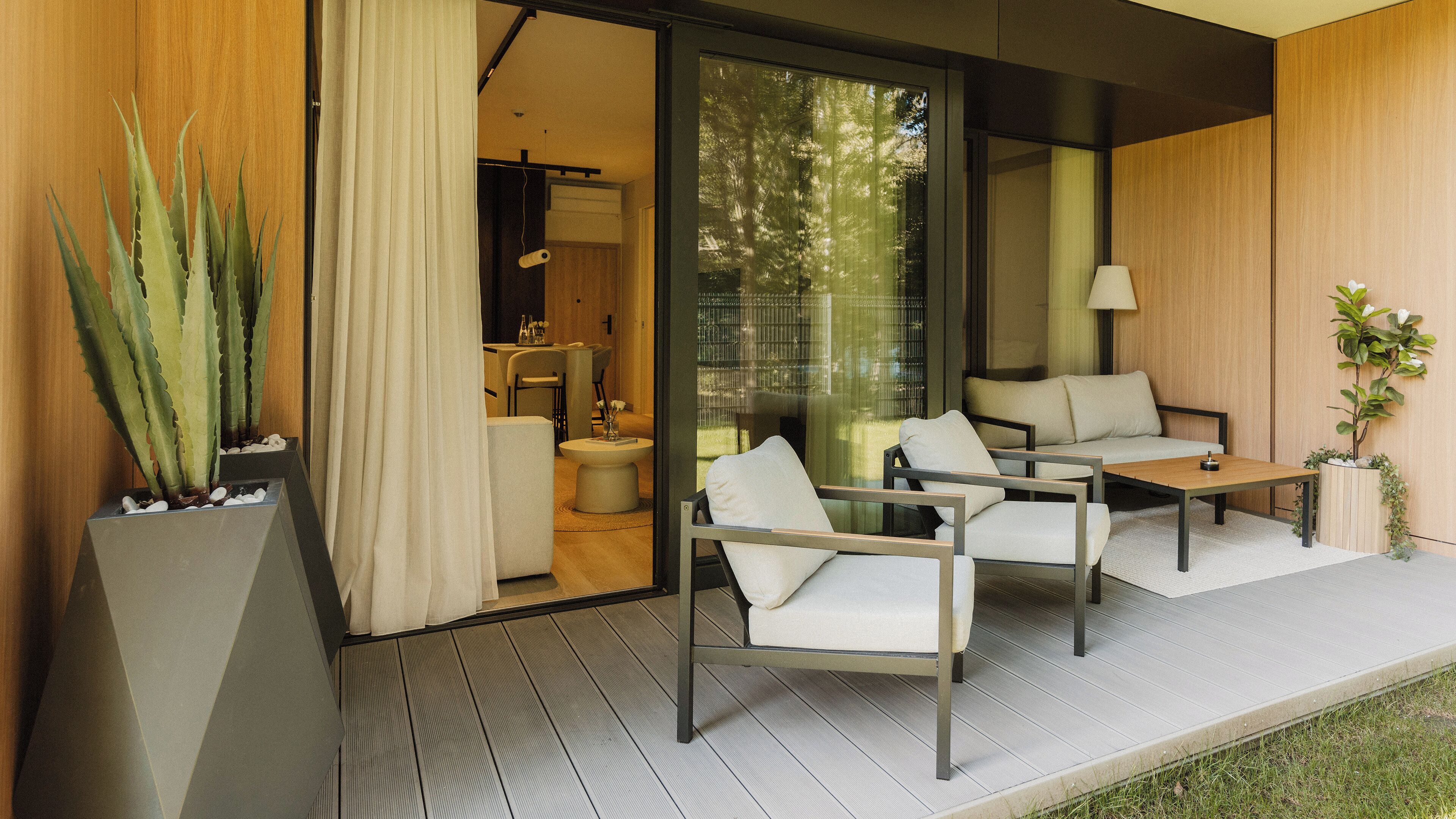 A modern outdoor seating area with a sofa and chairs, a small table, and a potted plant.