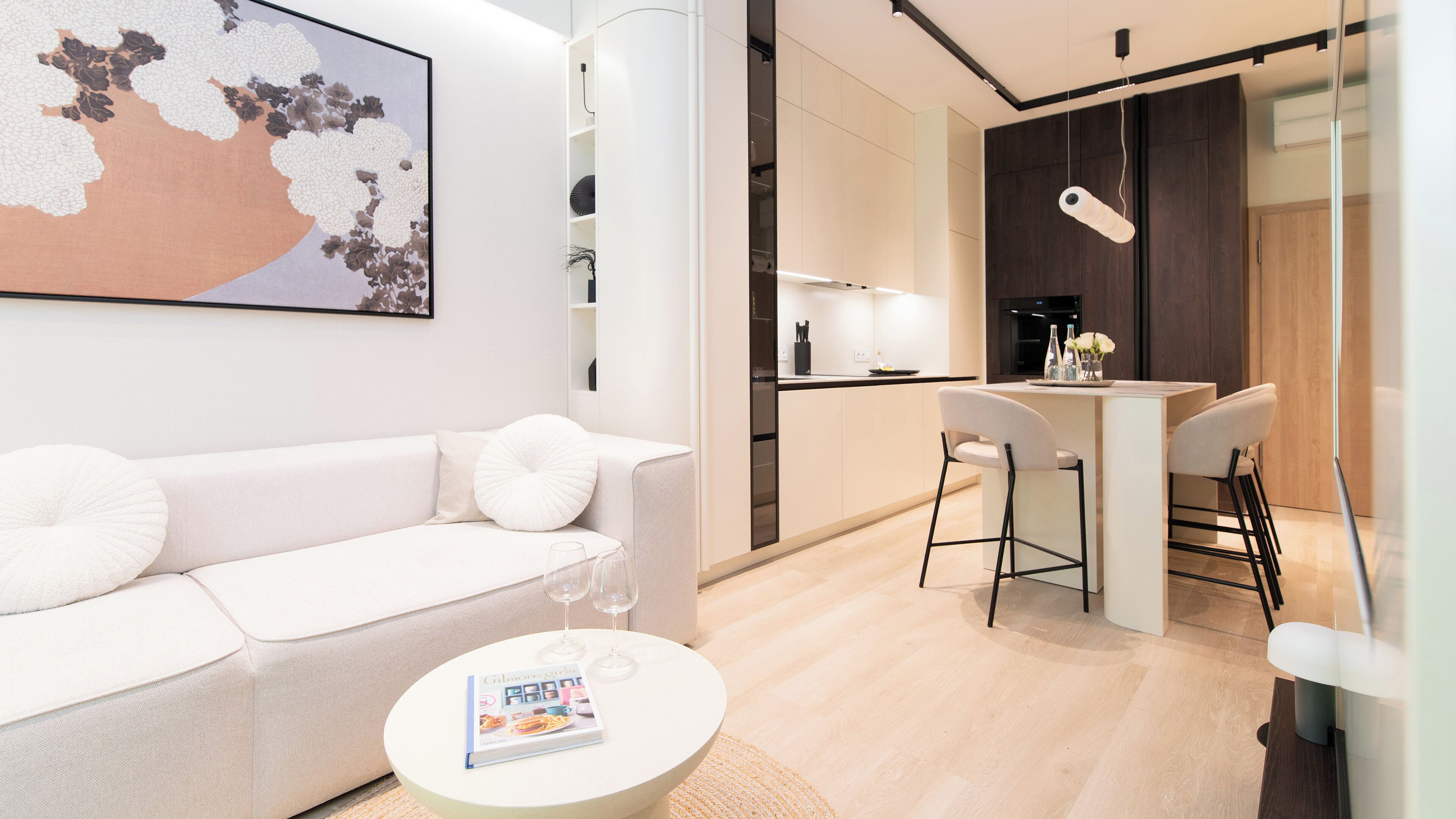 A modern living room with a white sofa, a round coffee table with a magazine, and a painting on the wall.