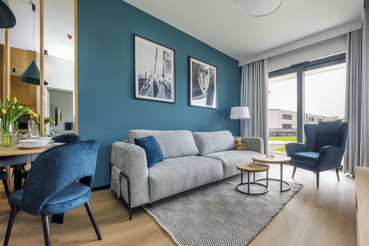 Un salon moderne avec un canapé gris, des fauteuils bleus, une table basse et un téléviseur.