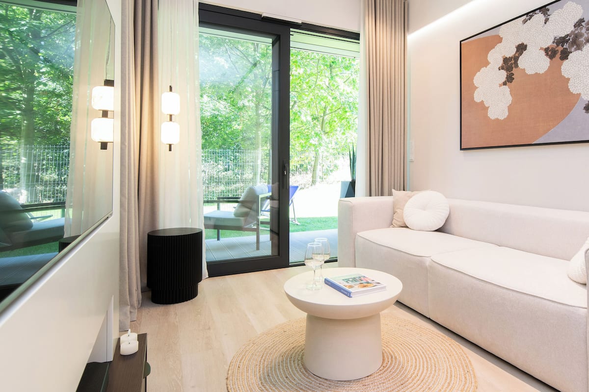 Un salon moderne avec un canapé blanc, une table basse ronde et une grande fenêtre donnant sur un paysage verdoyant.