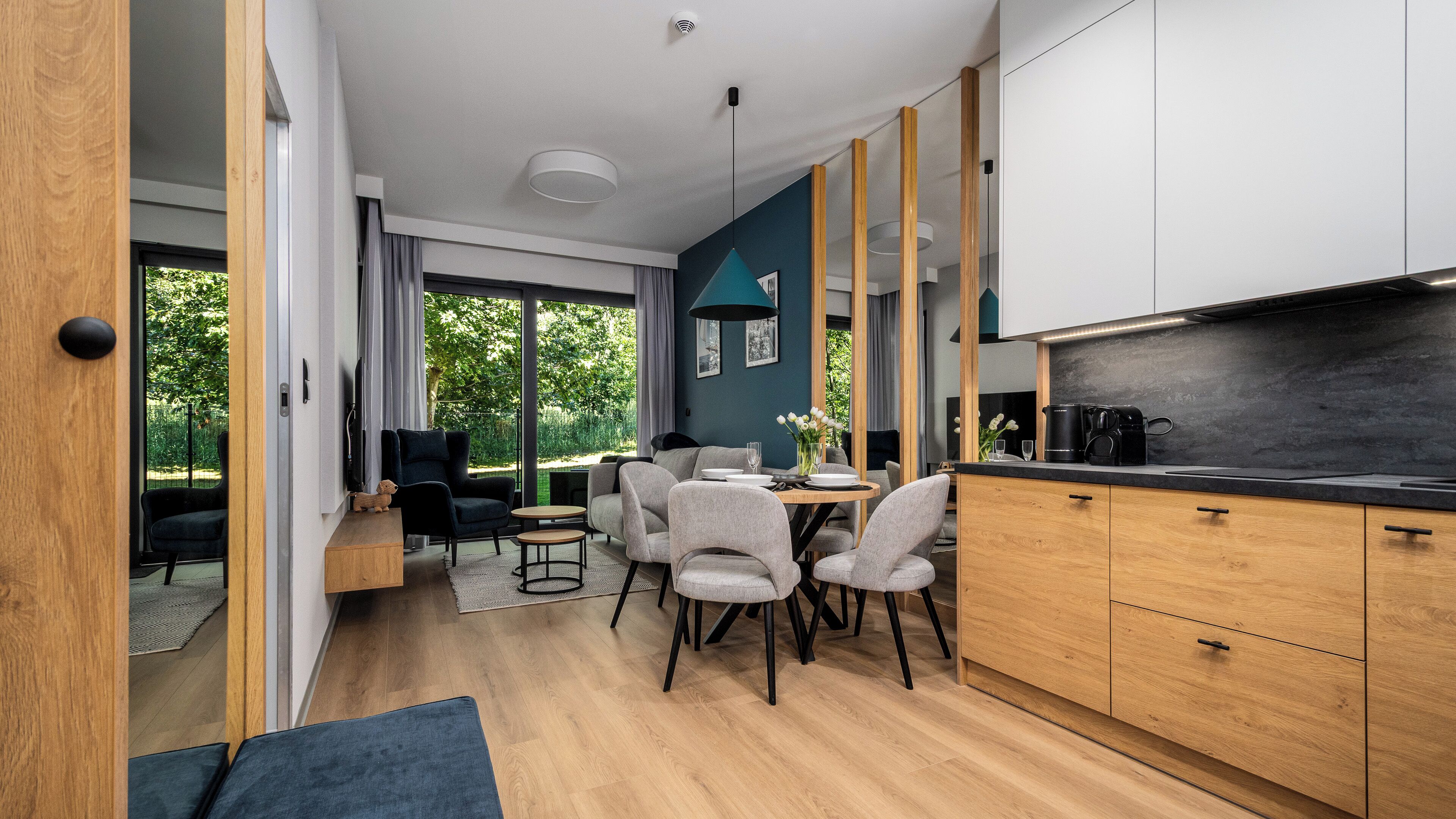 A modern kitchen with wooden cabinets, a black countertop, and a dining area with a round table and chairs.