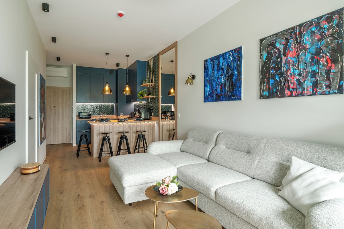 Un salon moderne avec un canapé d’angle gris, une petite table basse ronde et un coin repas avec une cuisine en arrière-plan.