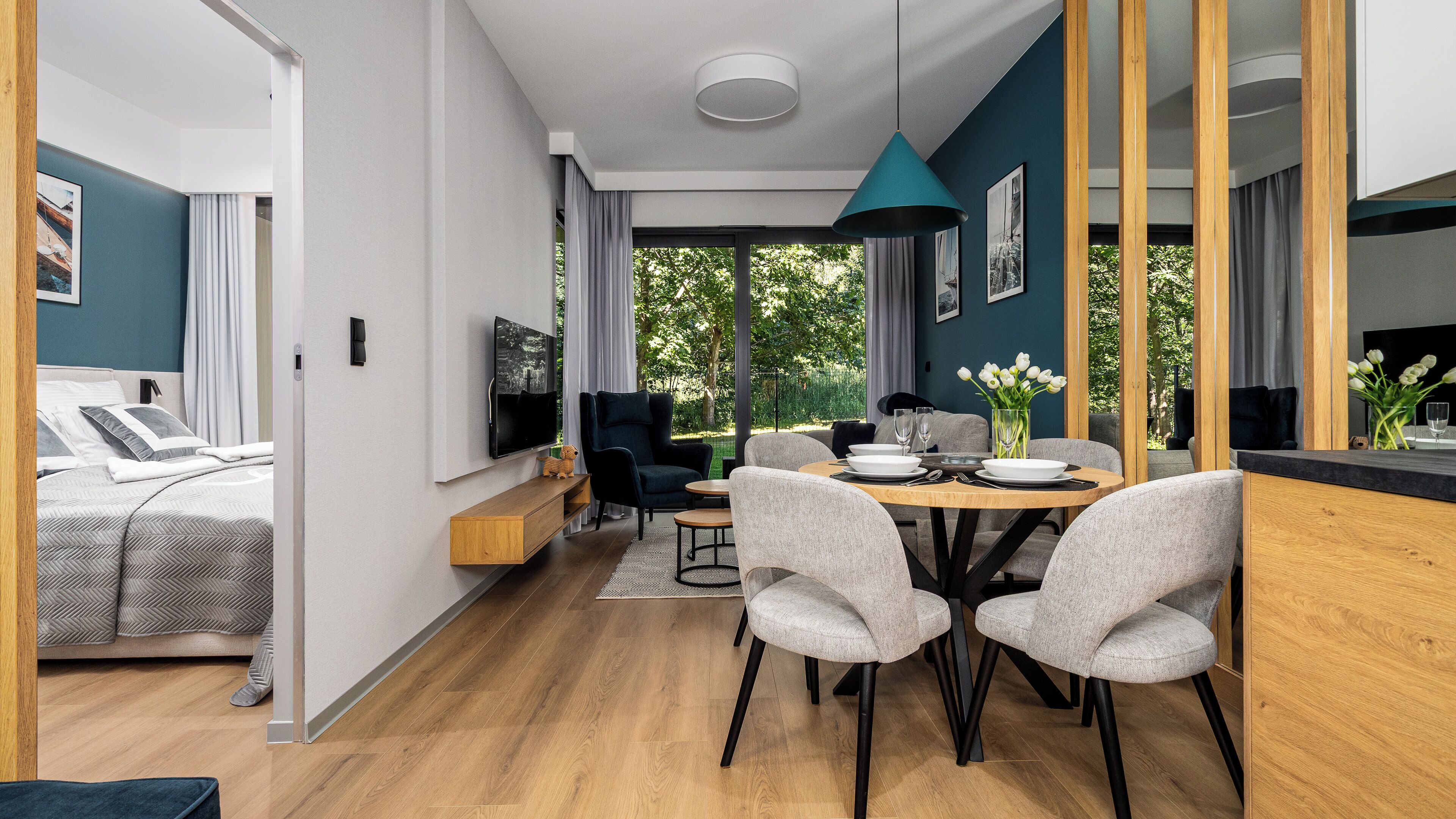 A modern, open-plan living space with a dining area, a sofa, and a TV mounted on the wall.