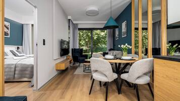 A modern, open-plan living space with a dining area, a sofa, and a TV mounted on the wall.