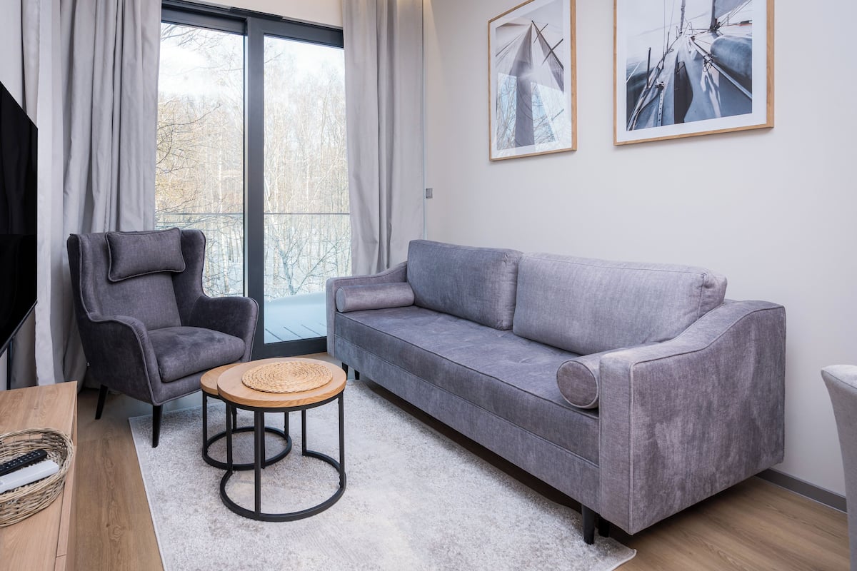 Un salon moderne avec un canapé gris, un fauteuil gris, un téléviseur à écran plat et deux tableaux encadrés accrochés au mur.